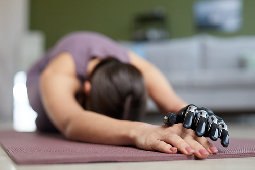 Close-up of young woman with prosthesis arm doing stretching exercises on exercise mat at home