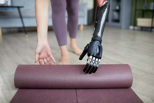 Close-up of young woman with prosthetic arm using exercise mat in her training at home