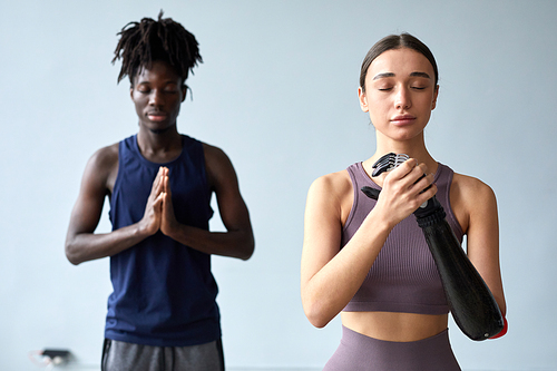 Young woman with disability meditating with her eyes closed together with young guy during yoga class