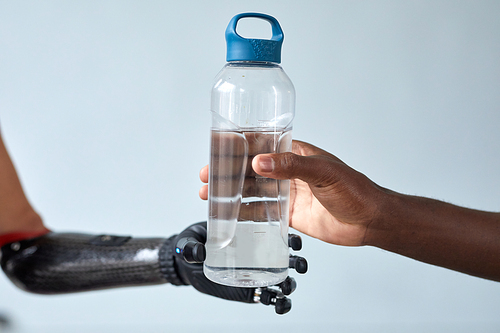 Close-up of African man giving bottle of water to woman with prosthetic arm isolated on blue background