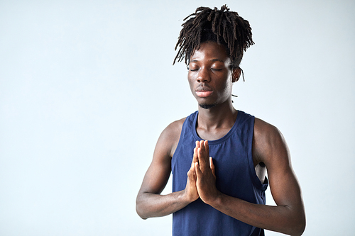 Portrait of African young man meditating with his eyes closed standing against blue background