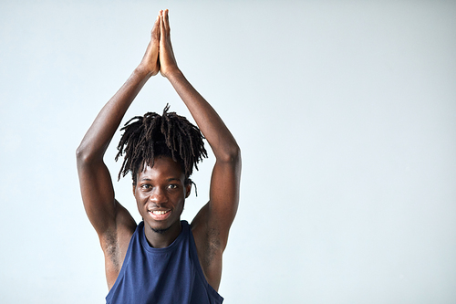 Portrait of African young man smiling at camera while doing yoga exercises against blue background