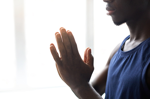 Close-up of African young man folding his hands and concentrating on meditation during yoga practice