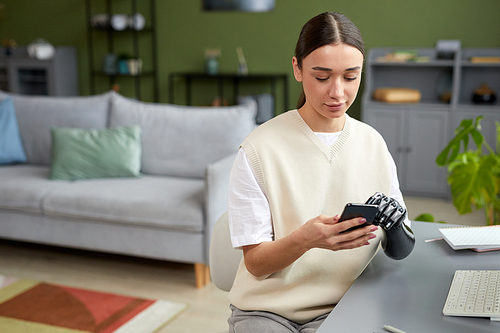 Young girl with prosthetic arm using her mobile phone while sitting at table in living room