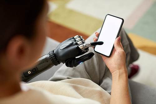 Close-up of young woman typing message on mobile phone with prosthetic arm while sitting on sofa