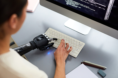 High angle view of woman with disability writing codes on computer, sitting at her workplace and typing on keyboard