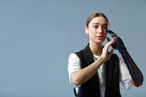 Portrait of young woman with prosthetic arm looking at camera standing on blue background