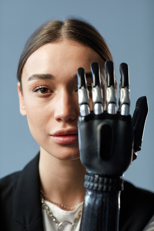 Portrait of young girl looking at camera through prosthetic arm isolated on blue background