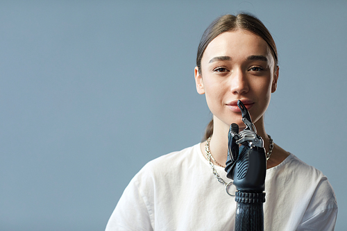 Portrait of young woman with disability having prosthetic arm looking at camera against blue background