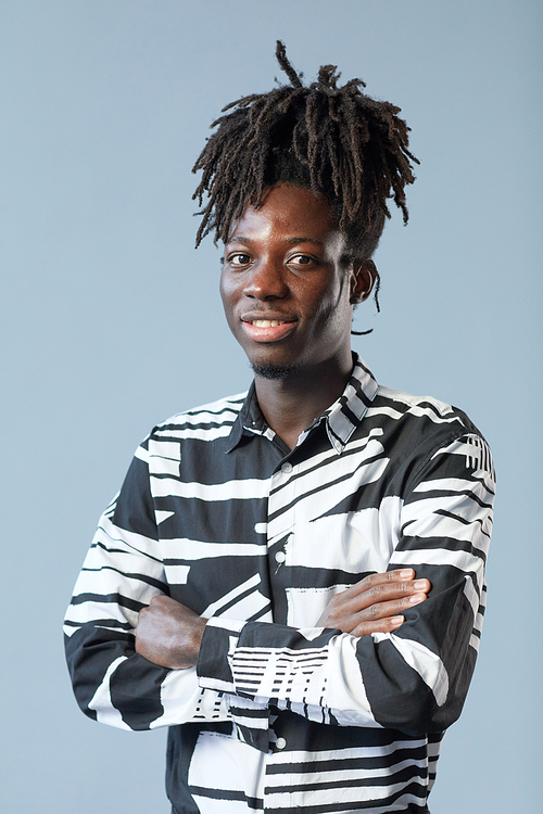 Portrait of African guy with fashion hairstyle standing with his arms crossed and smiling at camera on blue background