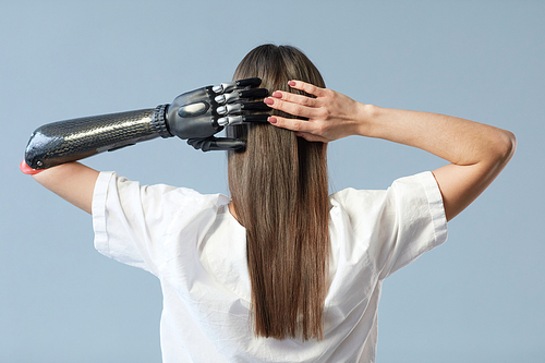 Rear view of young girl with prosthetic arm and long hair standing against blue background