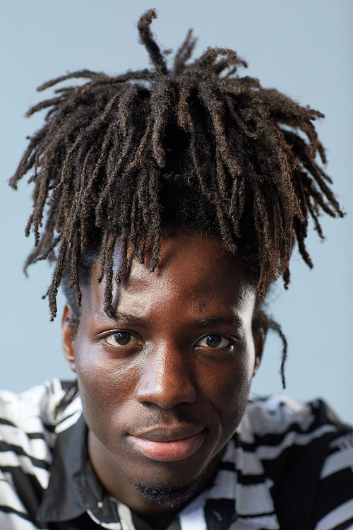 Close-up of African young guy with stylish hairstyle looking at camera on blue background