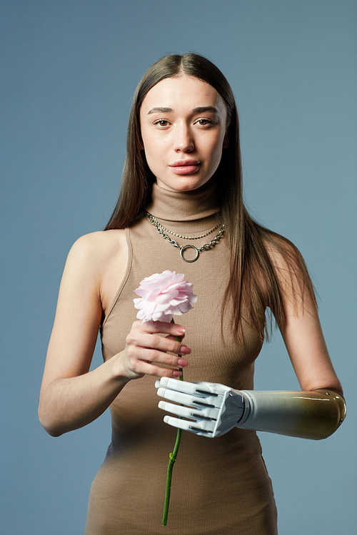 Portrait of young girl with prosthetic arm holding flower and looking at camera against blue background