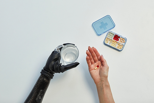 High angle view of young woman with disability holding glass of water and taking medicine