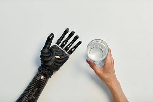 High angle view of young woman with prosthetic arm holding glass of water and drinking pill