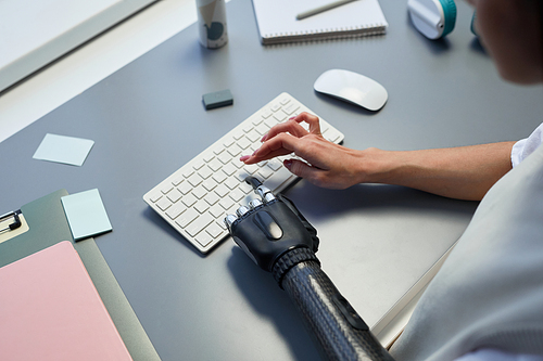 Close-up of woman with prosthetic arm typing on keyboard during her work on computer at table