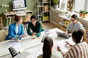 Group of businesswomen working in team at table using laptop and examining documents during meeting