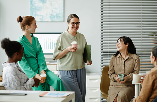 Group of colleagues talking and laughing together for cups of coffee during break at office