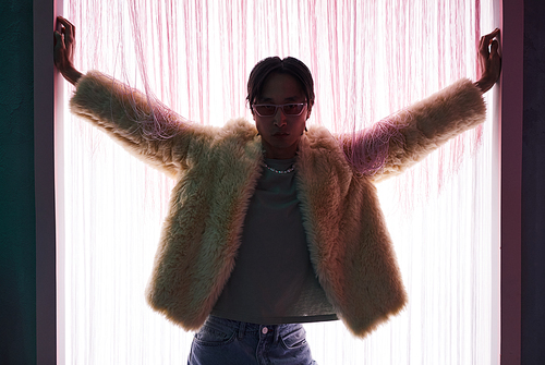 Backlit portrait of extravagant Asian man wearing fur coat entering stage at nightclub or dance party