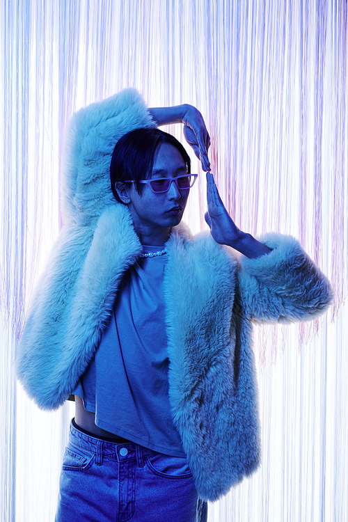 Waist up portrait of extravagant Asian man dancing vogue in blue neon light