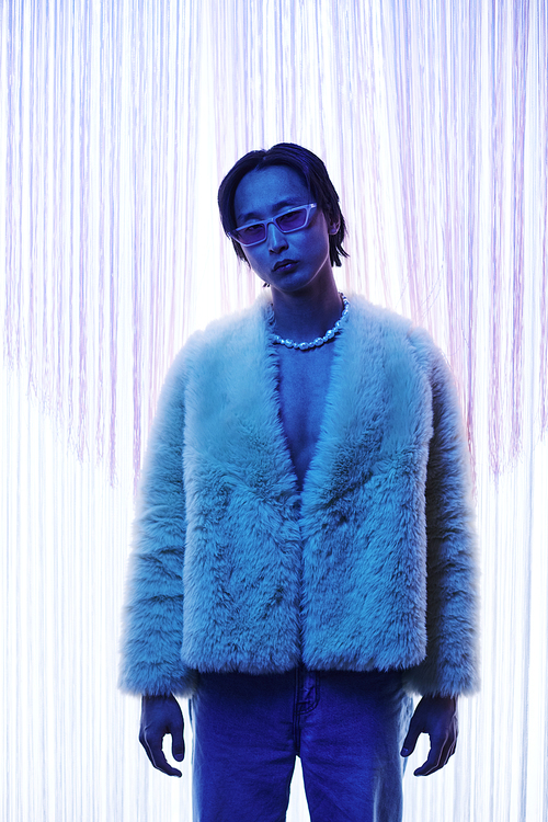 Vertical portrait of extravagant Asian man wearing fur coat at nightclub or party in blue light
