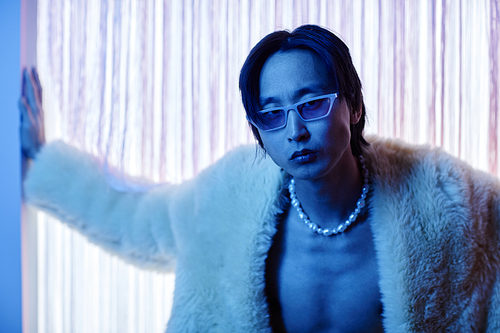 Portrait of handsome Asian man wearing party outfit and sunglasses looking at camera intensely in blue neon light