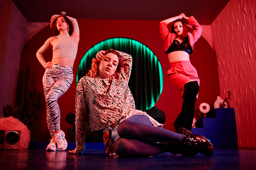 Full length shot of group of girls dancing vogue in red neon light and looking at camera