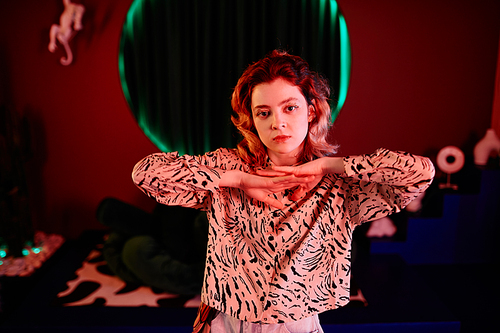 Waist up portrait of young woman dancing vogue style in red neon light and looking at camera