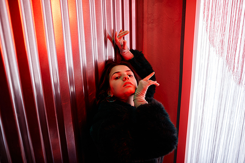 High angle portrait of sensual young woman dancing vogue style in red neon light and looking at camera, copy space