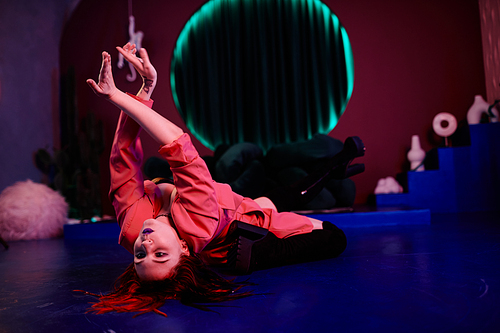 Portrait of young woman dancing vogue style in club and doing sensual floor performance in red neon light, copy space