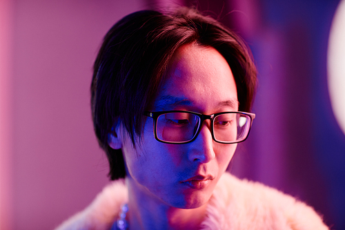 Closeup potrait of young Asian man in nightclub lit by pink neon lights and looking away