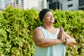 Waist up portrait of overweight mature woman holding hands together and medtating outdoors, copy space