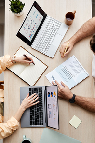 Above view of hands of two young students sitting in front of laptops with financial data on screens and analyzing diagrams and charts