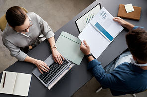 Above shot of two young economists sitting by workplace in front of laptops and working with financial information and documents