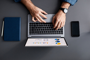 Above shot of hands of young businessman over laptop keyboard and touchpad during analysis of financial diagrams and chart