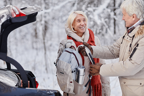 Waist up portrait of smiling senior couple taking out hiking backpack while enjoying winter getaway in nature together, copy space