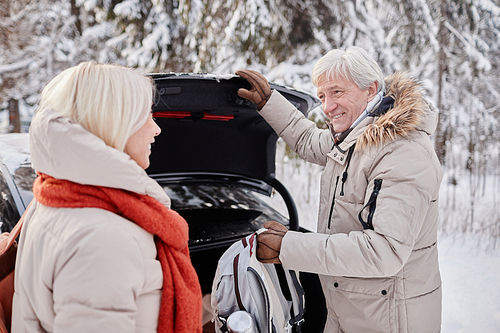 Waist up portrait of smiling senior couple opening car trunk while enjoying winter getaway in nature together, copy space