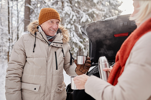 Waist up portrait of happy mature couple enjoying cup of hot coco outdoors during winter hike