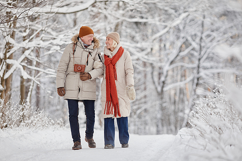 Full length portrait of happy senior couple enjoying walk in winter forest and looking at each other with love, copy space