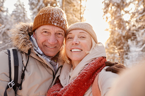 POV portrait of happy senior couple taking selfie photo while enjoying hike in winter forest