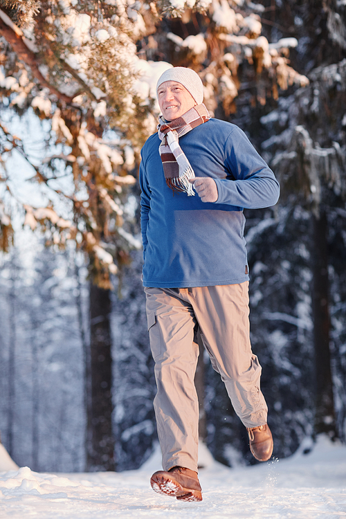 Vertical full length portrait of sportive senior man running in winter forest