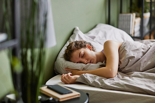 Young woman sleeping on pillow under blanket in her bed in bedroom after hard day