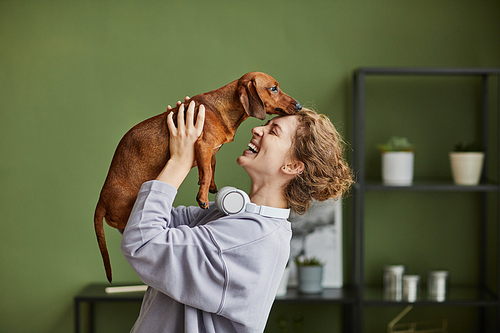 Happy young owner playing with her little dog standing in the room at home