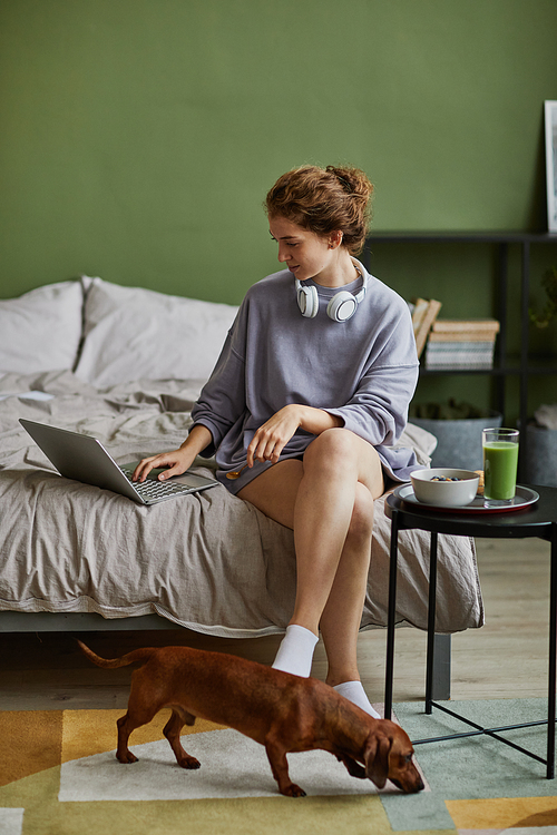 Girl sitting on bed and using laptop while having breakfast in the morning