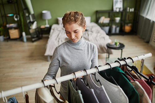 Young woman choosing clothes on the rack standing in her room, she going to work in the morning