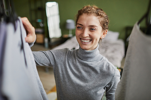 Young happy girl choosing suits on rack in her room, she preparing for work in the morning