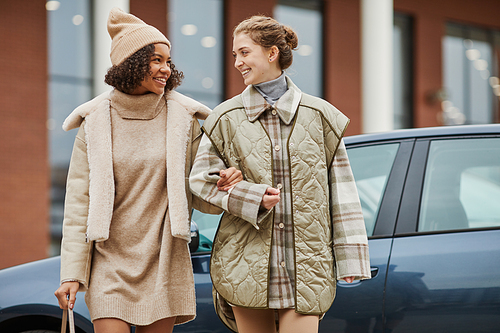 Two girls in warm clothing walking together in the city, they talking and smiling