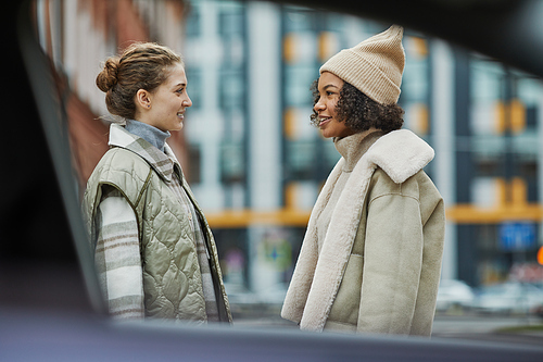 Two friends in warm clothing talking to each other while meeting in the city