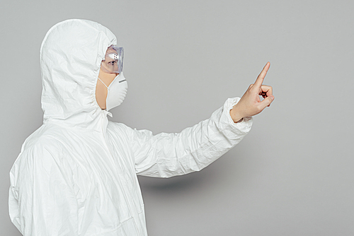 side view of asian epidemiologist in hazmat suit and respirator mask showing warning gesture on grey background