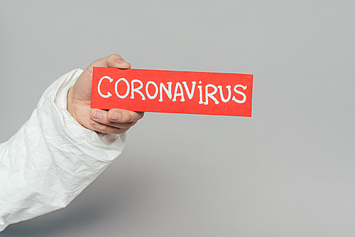 cropped view of epidemiologist holding warning card with coronavirus inscription on grey background